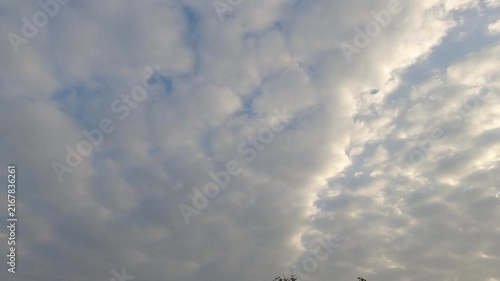 Beautiful video of soft fluffy white clouds moving slowly across a bright blue sky. Peaceful natural cloudscape background with warm sunlight peeking through.