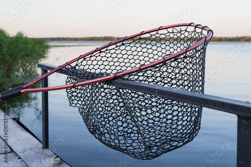 A large landing net is prepared on a lakeside pier for lifting caught fish, representing recreational fishing equipment and outdoor leisure.