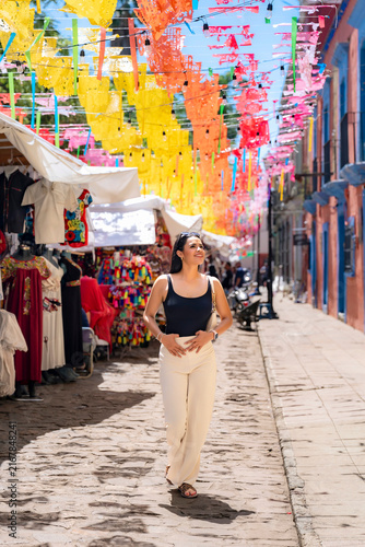 Принти на полотні Latina woman walking along a cobblestone street adorned with colorful papel pica