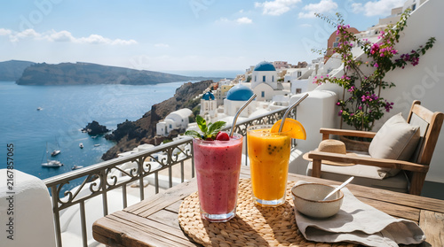 Two colorful fruit smoothies on wooden table overlooking beautiful caldera of Santorini island Greece travel.