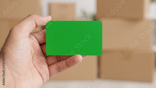 Hand Holding a Blank Green Screen Card for Custom Messaging and Copy Space with Blurred Cardboard Boxes in Background