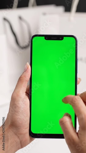 Woman hands using smartphone with green screen mockup for online shopping app in front of shopping paper bags