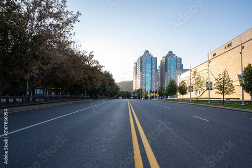Wide empty asphalt road with yellow double lines and modern city buildings under clear blue sky in Almaty city, Kazakhstan. Almaty, Kazakhstan. 