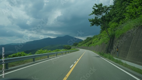 Empty mountain road curve with yellow center line leading to scenic peaks under cloudy dramatic sky travel background
