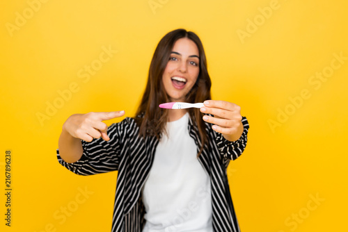 Foto Happy young woman joyfully pointing at a positive home pregnancy test, celebrati