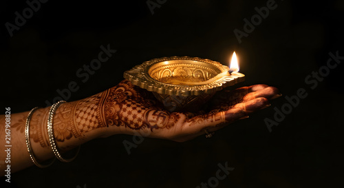 Hand with henna holding a traditional lit diya lamp for diwali festival