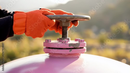 Worker in Orange Gloves Turning a Valve Wheel on a Pink Industrial Tank in Outdoor Environment