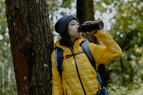 Nature, health and young asian woman hiking and drinking water on adventure trail with trees in summer. Close up Female in forest with a drink of water standing in natural landscape.