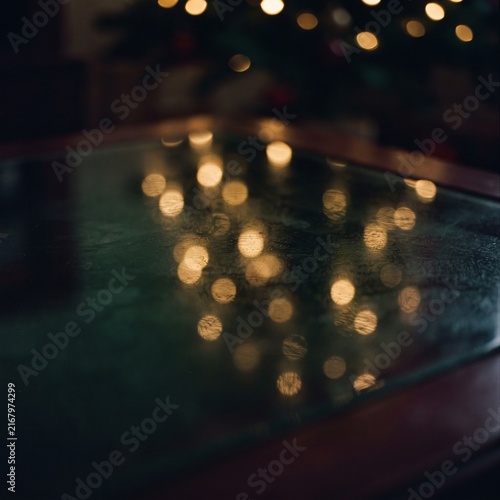 Warm glowing fairy lights reflected on dark polished glass surface, magical festive Christmas bokeh evening holiday background.