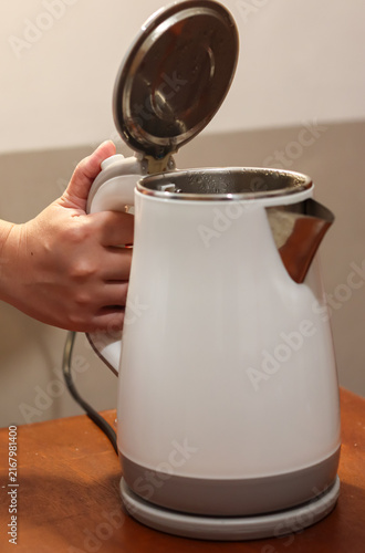 Woman's hand pressing the lid release button of an electric kettle after the water has boiled, opening the kettle to check the hot water inside
