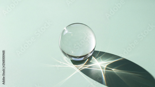 Glass sphere casting shadow with light reflections on smooth surface creating abstract