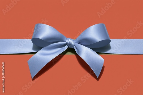 Lavender satin ribbon tied in a bow on a coral red surface, featuring a smooth texture and soft lighting for gift packaging and banners