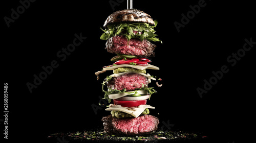 Exploded burger with stacked ingredients floating against black background beef patty cheese slice