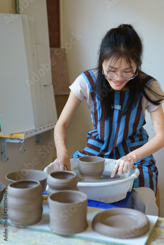 asian female ceramic artist wearing apron cutting clay bowl from pottery wheel using string, traditional handmade pottery process in creative studio with focus on craft and artistic lifestyle
