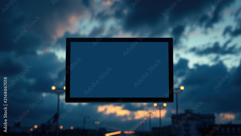 Fototapeta premium Billboard against dramatic sky. Dark silhouette buildings visible below. Bright sunset colors illuminate clouds. Empty screen awaits message.