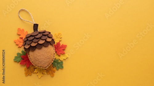 A handmade felt acorn ornament decoration with colorful fabric autumn leaves on a warm yellow background for a festive fall season concept