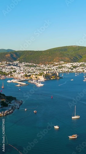 Vertical video. Bodrum, Turkey. Aerial drone view of Bodrum Marina filled with yachts and sailboats, with the historic Castle of St. Peter commanding the coastline and whitewashed houses cascading ac