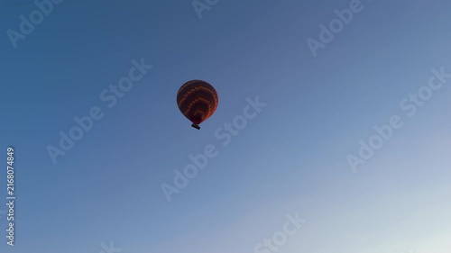 Goreme, Nevsehir, Turkey. A single large checkered hot air balloon in vibrant yellow, red, orange and purple stripes floating in a clear morning blue sky, low angle view with ample copy space. Aerial