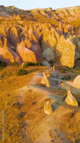 Vertical video. Goreme, Nevsehir, Turkey. Devrent Valley fairy chimney formations, aerial panoramic view at golden hour sunset over eroded volcanic tuff landscape. Aerial View. Rich colors