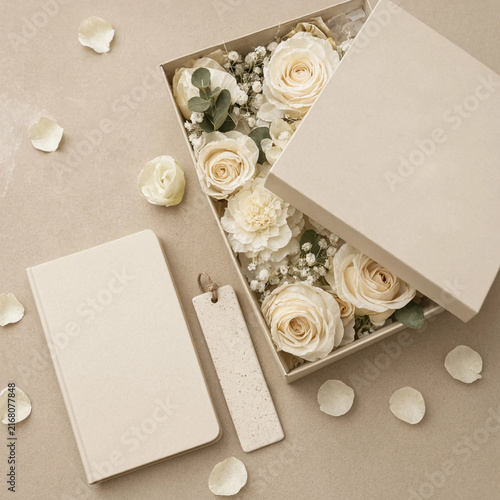 Elegant gift box with cream roses, a notebook, and a bookmark on a beige background