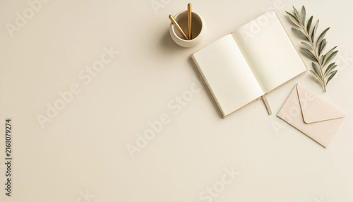 Open notebook with pens, envelope, and olive branch on a beige background