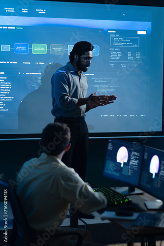 Indian Male Engineer Discussing System Monitoring Dashboard During Software Development Meeting. Developer Presenting Technical Results and Programming Strategy to Colleagues.