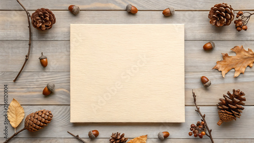 Blank kraft paper card on rustic wooden table with autumn pinecones and leaves for seasonal crafting and design