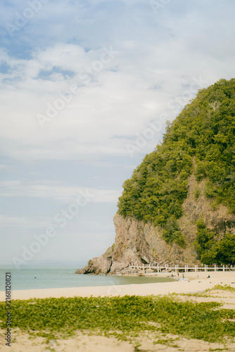 Tropical green cliff and headland along the ocean shoreline under a soft sky.