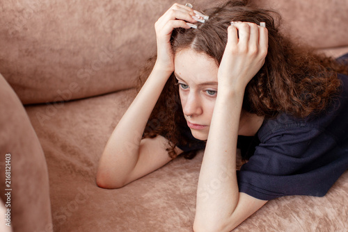 Obraz na płótnie Young woman lying on sofa holding head with hands looking sad and stressed