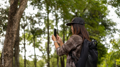 Fotografía A woman stands in a park surrounded by trees while using her smartphone to take a picture