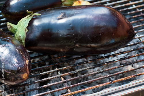 Close-up of fresh purple eggplants grilling on a hot metal barbecue grate outdoors