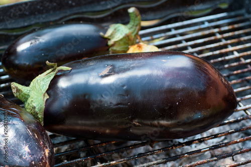 Close-up of fresh whole purple eggplants grilling on a hot metal barbecue grate