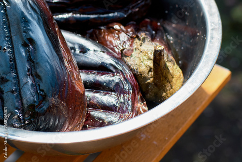 Close-up of freshly grilled eggplants resting inside a metal bowl on a wooden surface.
