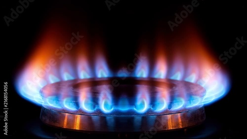Close-up of a gas stove burner with blue and orange flames igniting in the dark.