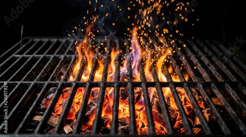Glowing charcoal embers burning bright with vibrant orange flames underneath a heavy black metal barbecue grill