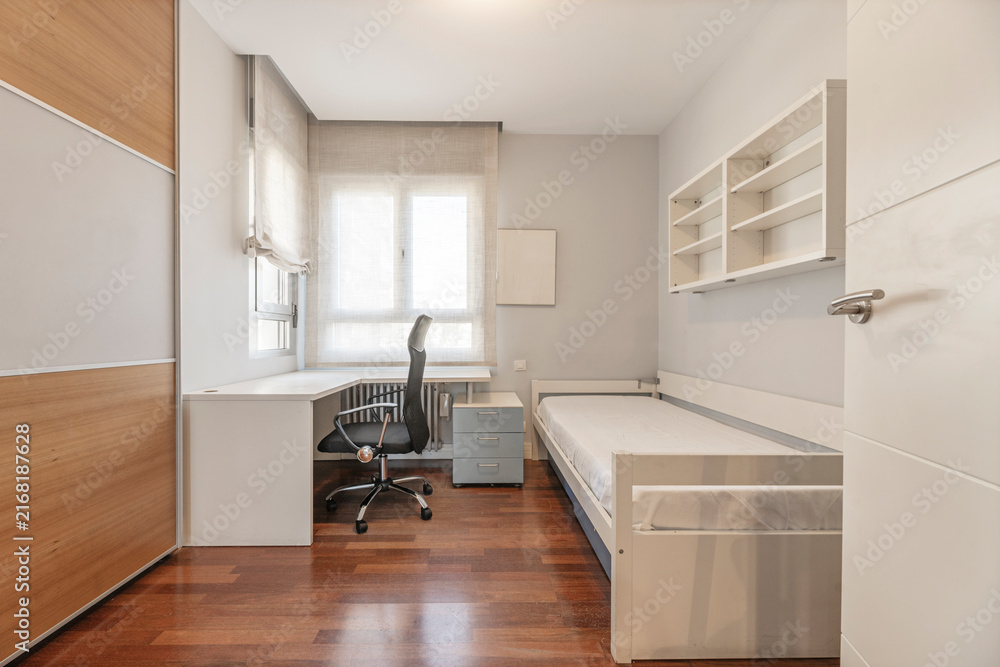 Fototapeta premium Compact single bedroom with corner desk, mesh office chair, twin bed, and open shelving above a drawer unit.