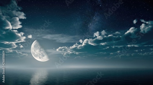 Glowing half moon shines brightly above the calm dark ocean water under a vast starry sky