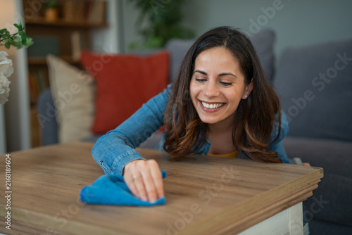 Bild auf Leinwand Smiling woman cleaning wooden coffee table at home