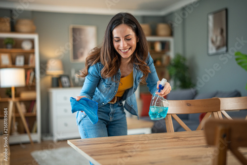 Foto Woman smiling cleaning living room table with spray bottle