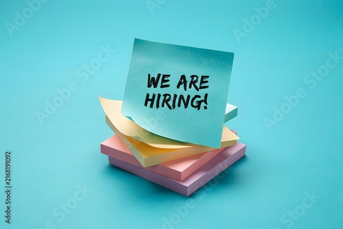 A 3d render of a stack of colorful sticky notes with the text we are hiring on a bright turquoise background, symbolizing recruitment and job search opportunities.