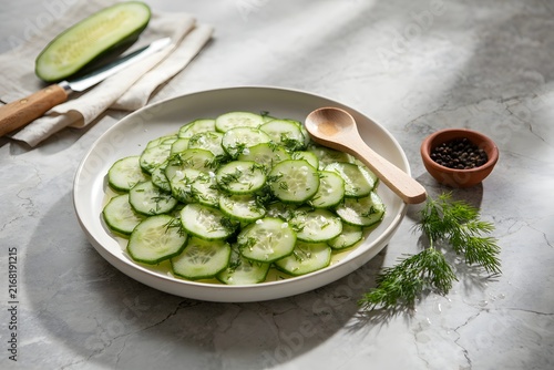 A fresh cucumber salad with dill and spices served on a ceramic plate, accompanied by a wooden spoon, capturing a healthy and delicious homemade vegetarian meal.