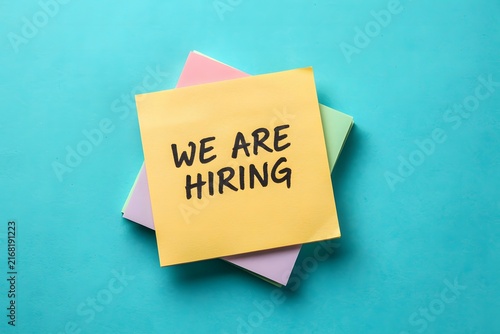 An overhead studio shot of a stack of colorful sticky notes on a vibrant blue background, with the text we are hiring clearly written for recruitment advertising.