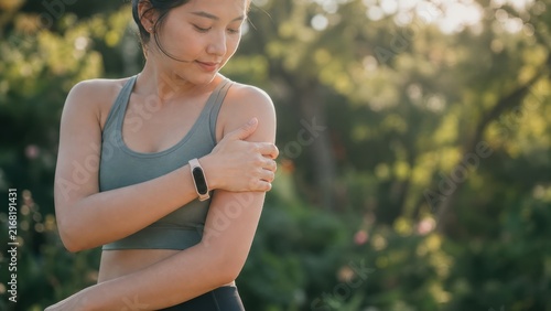 Fit young woman checking sore arm muscle while wearing fitness tracker after outdoor workout