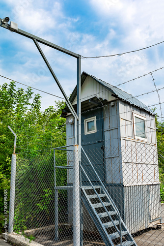 Security guard booth with a surveillance camera in a fenced area.