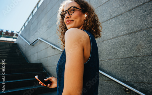 Young woman ascends stairs holding a smartphone during city commute