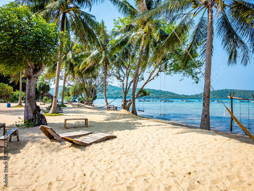 Alano Beach Karimunjawa showcasing a serene tropical landscape with golden sand, swaying palm trees, beach chairs, swings, and a hammock beside the clear blue ocean