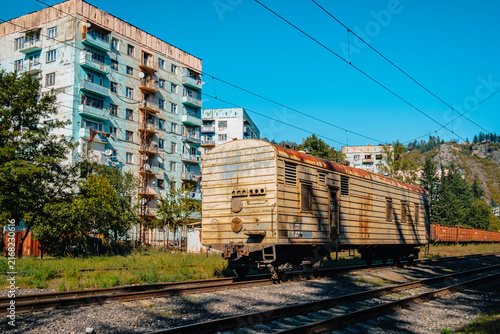 Fotografía Rusty railway wagon beside a Soviet-era Brezhnevka apartment block near the abandoned station in Chiatura, Georgia