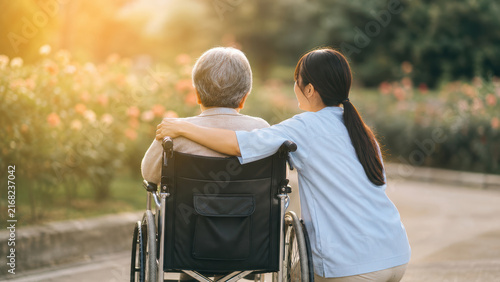 Caregiver walking with senior in wheelchair in garden at sunset, elderly care support
