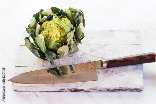 Green cauliflower and knife on chopping board