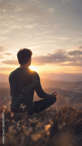 Man meditating on mountain top at sunrise practicing mindfulness and inner peace